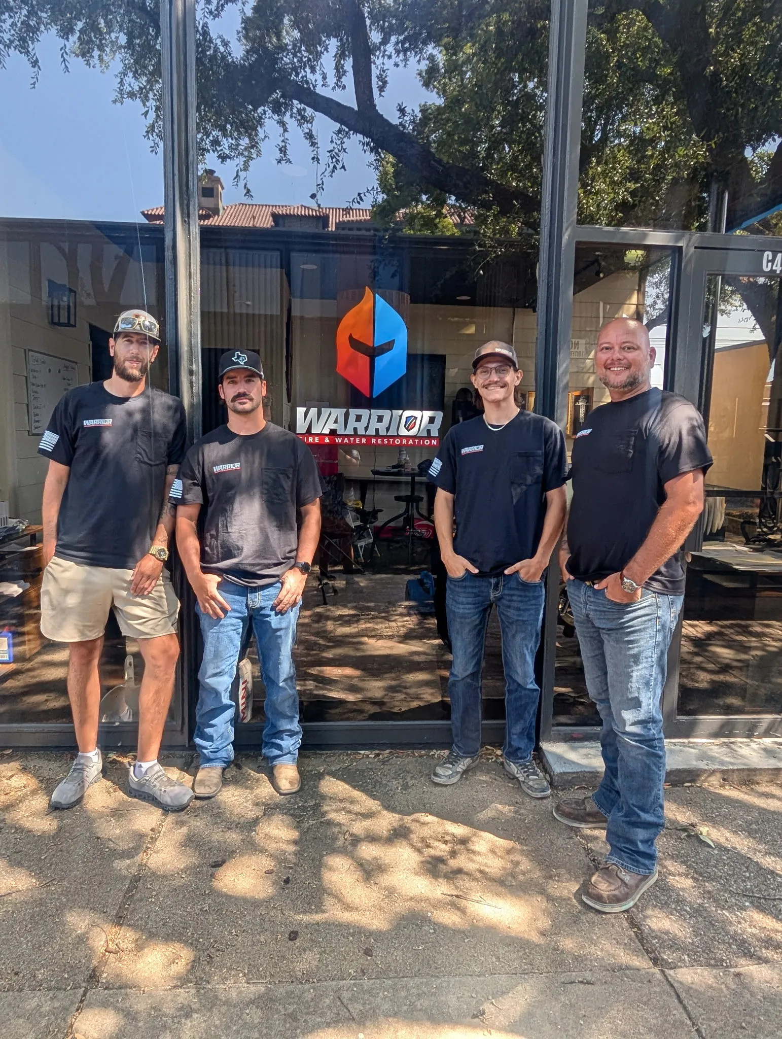 Four Warrior Restoration team members standing outside a glass door with the company logo.